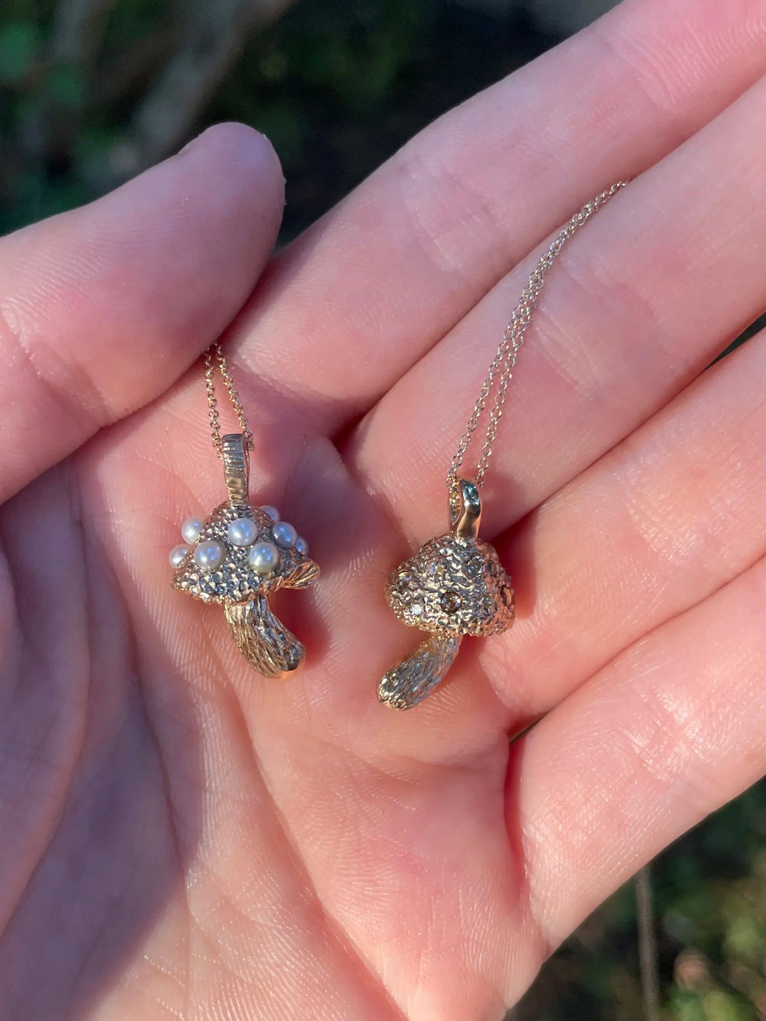 Gold earrings held in a hand with a blurred natural background