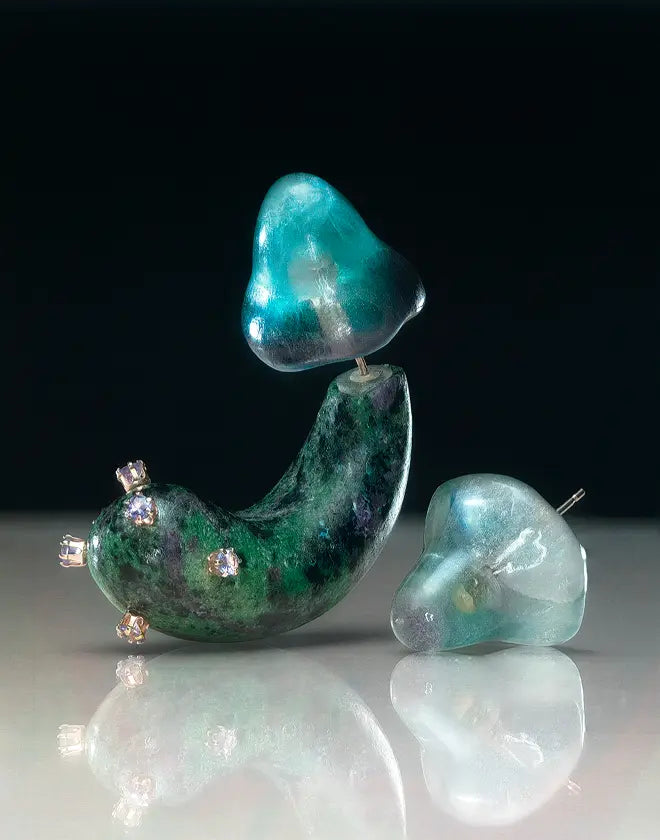 Teal and green glass sculpture with embedded crystals on a reflective surface.