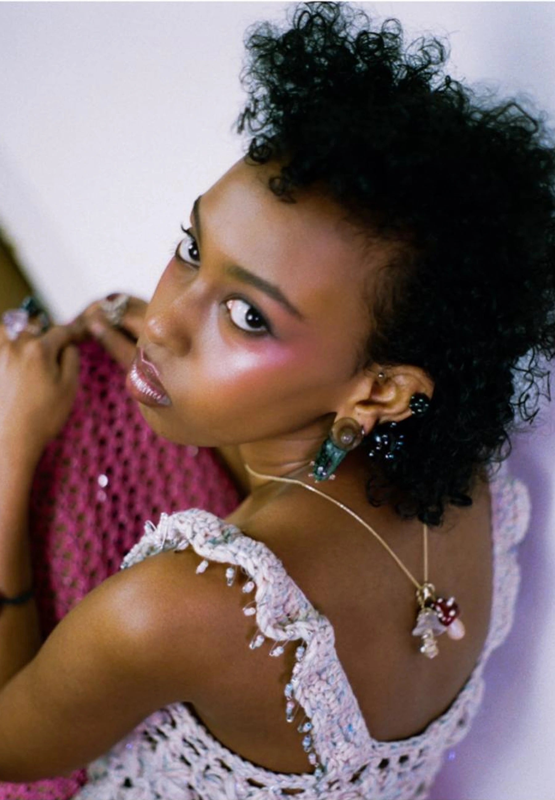 Woman with styled hair wearing a necklace with a pink background