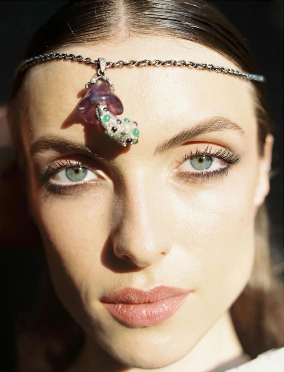 Close-up of a woman's face with a decorative headband featuring a purple gemstone.