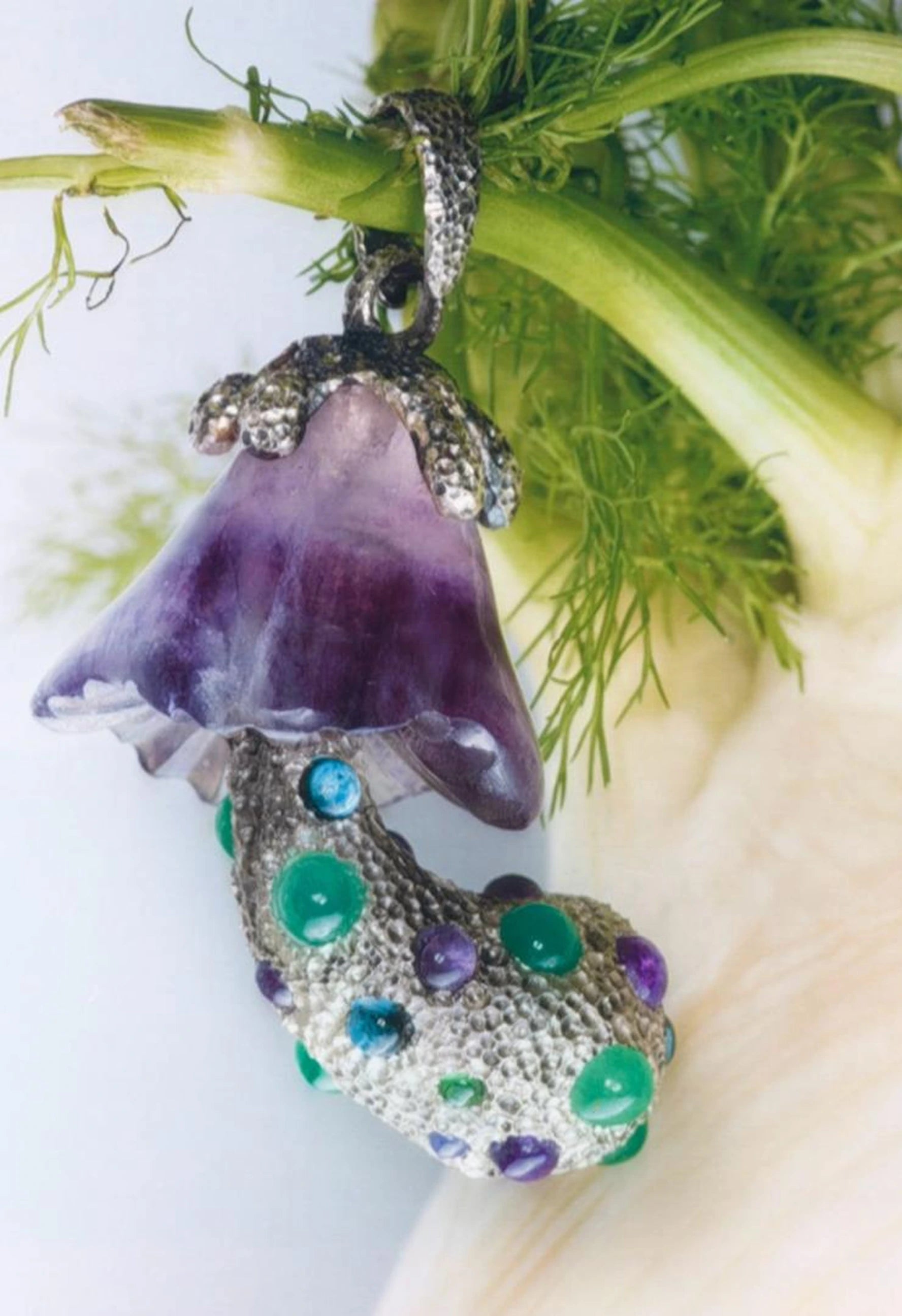 Jewelry pendant with purple and green gemstones on a white background
