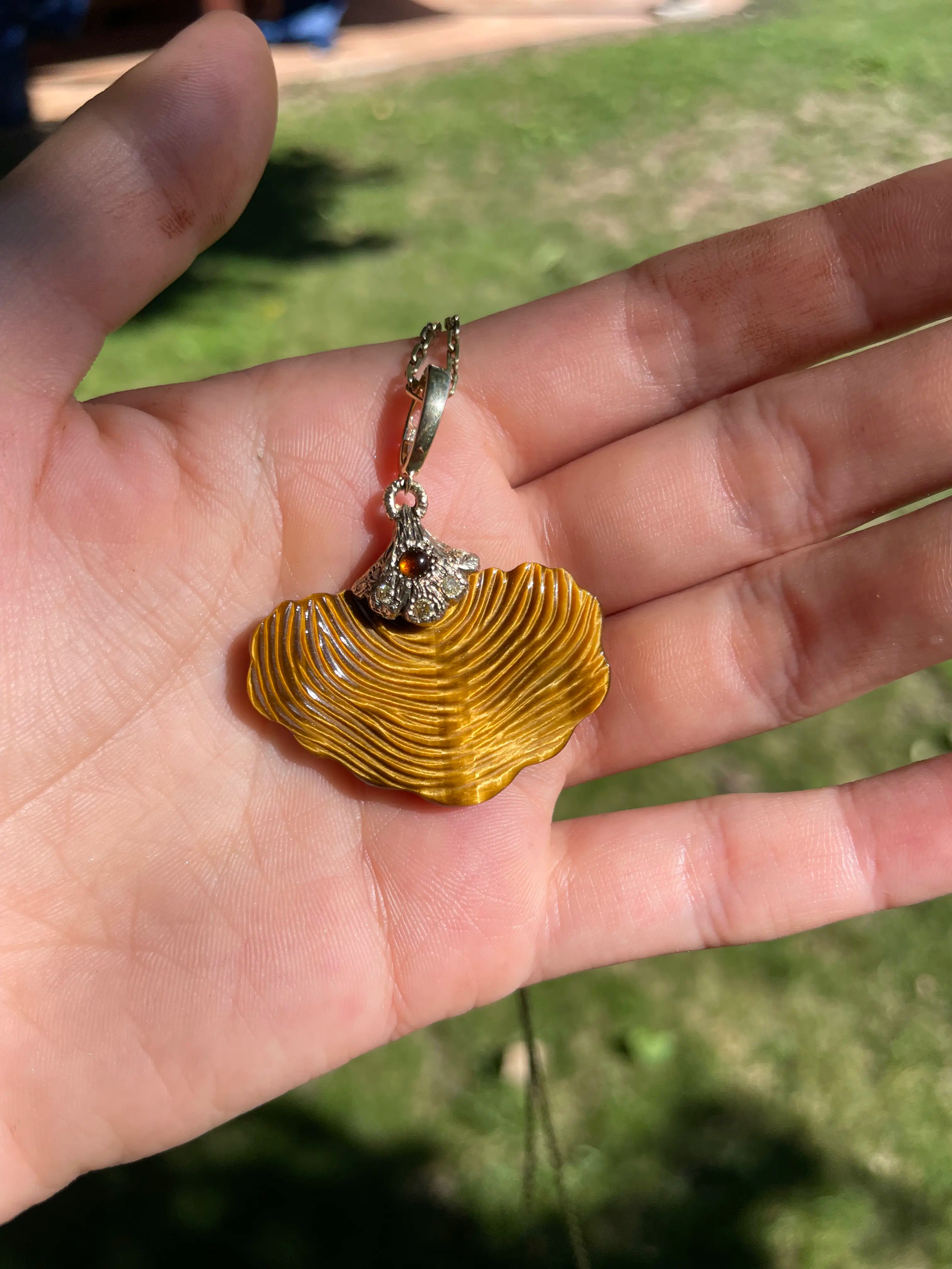 Gold shell pendant with a small decorative item held in a hand outdoors.