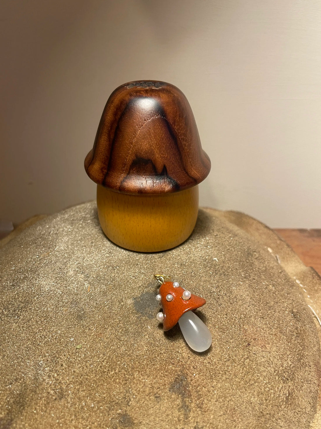 Wooden mushroom-shaped object on a textured surface with a smaller mushroom-shaped pendant.