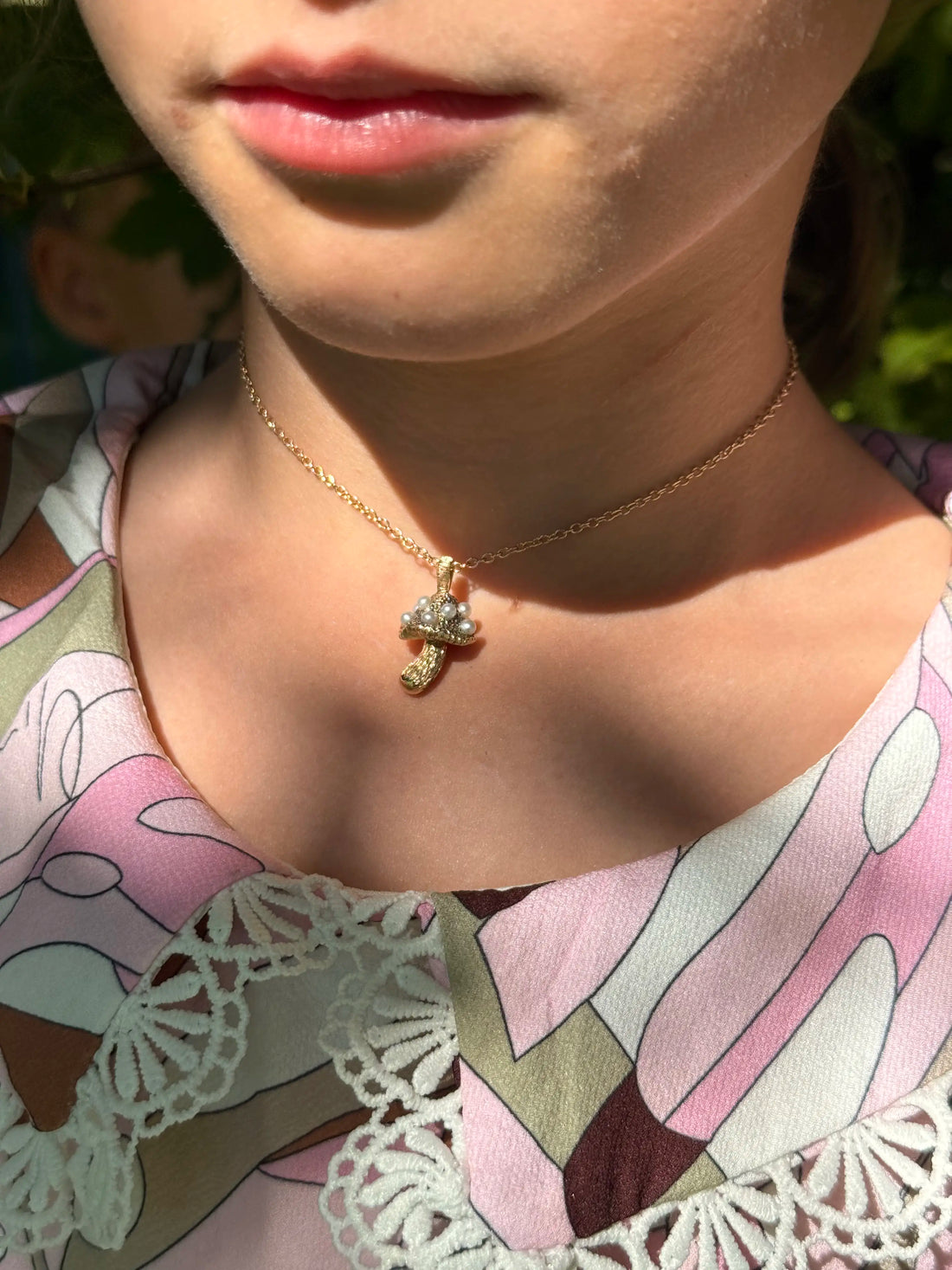 Close-up of a person wearing a gold necklace with a pendant, outdoors.