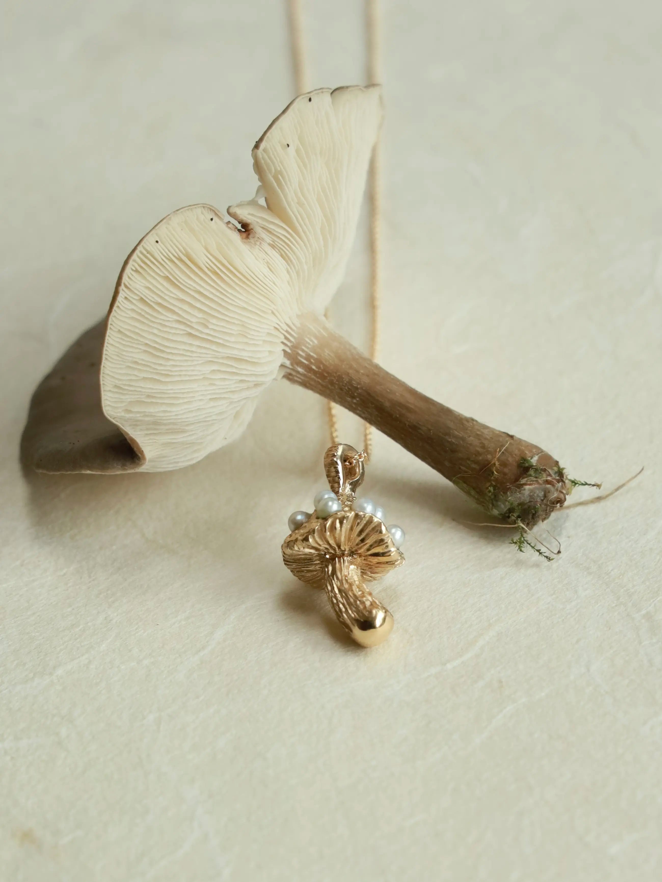 Gold pendant with a pearl on a mushroom-shaped stand against a beige background