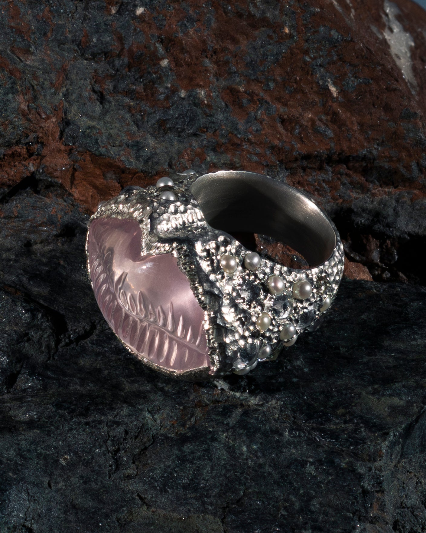 Silver skull ring with pink gemstone on a dark stone surface