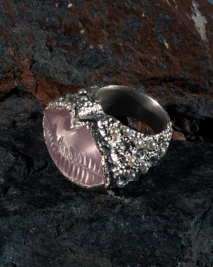 Silver skull ring with pink gemstone on a dark stone surface