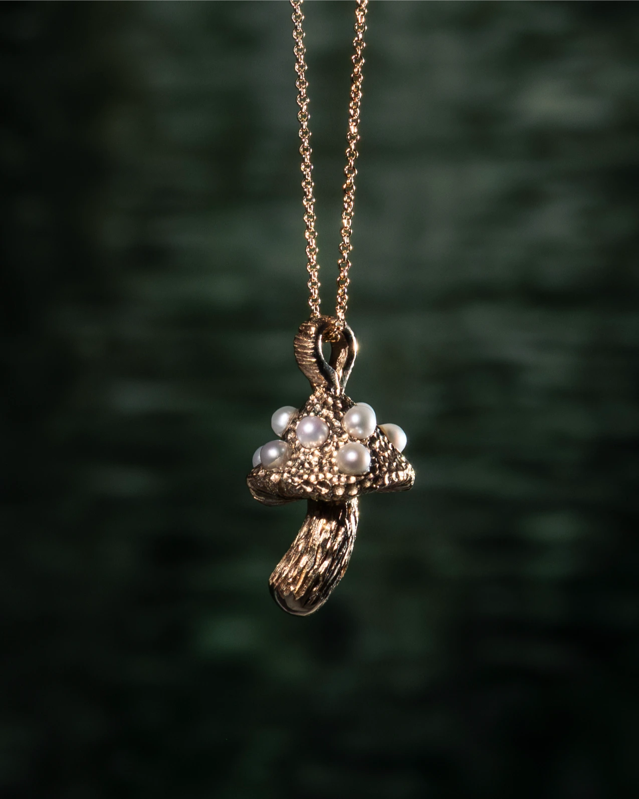 Gold mushroom-shaped pendant with pearls on a chain against a dark green background