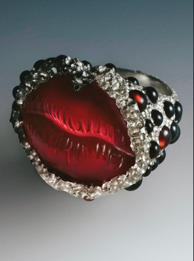 Ring with red central stone and black and silver accents on a gray background